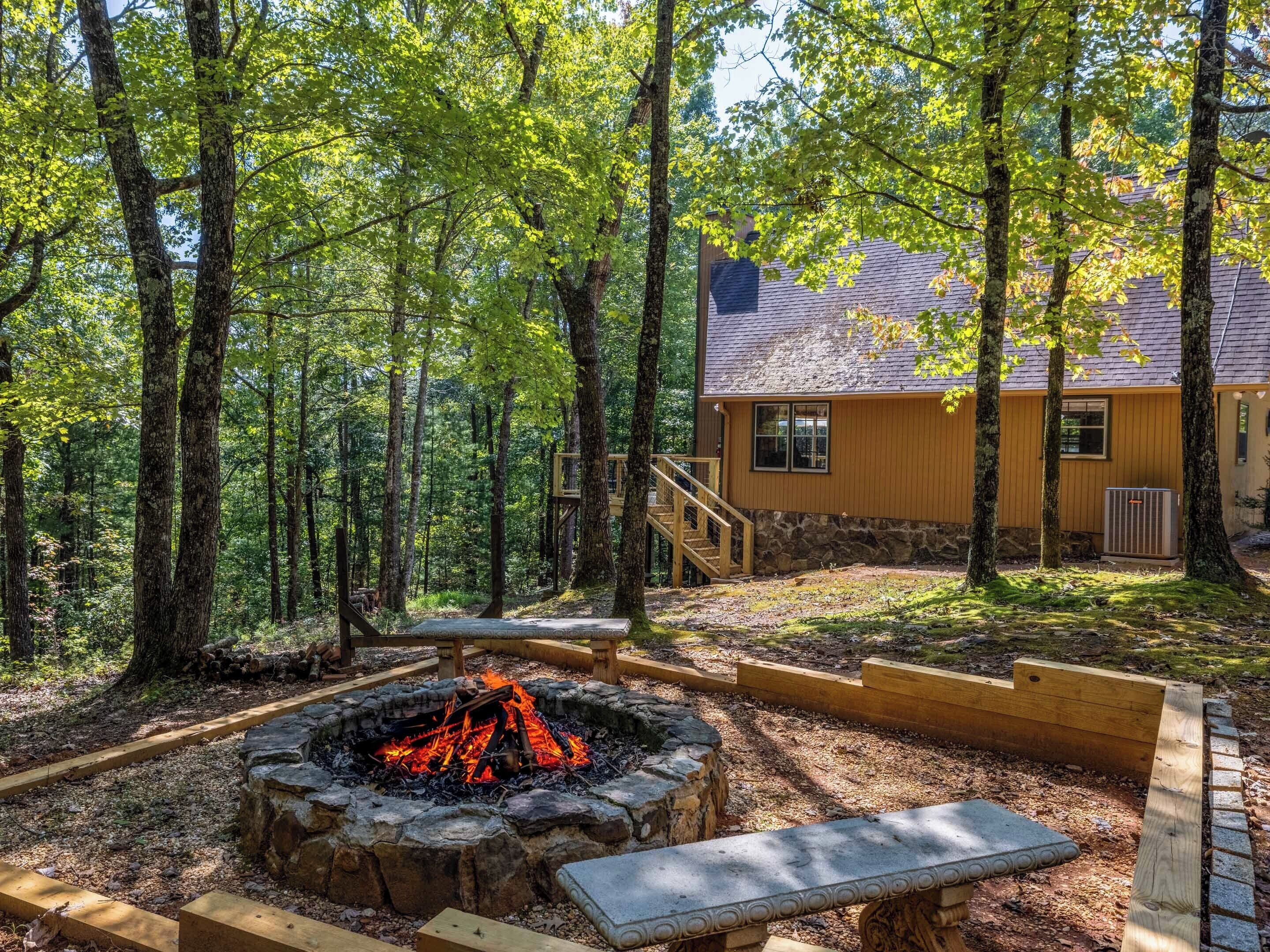 A cabin with a stone foundation, wooden deck, and a fire pit surrounded by a stone fire ring.