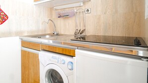 Una cocina compacta con armarios de madera, lavadora incorporada y un lavamanos de acero inoxidable.