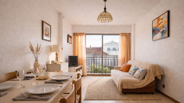 Un comedor con una mesa dispuesta para cuatro personas, un sofá, un televisor y un balcón con vistas a edificios.