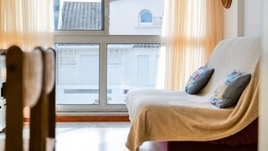 Habitación con sofá frente a un ventanal, cortinas y vistas de edificios.