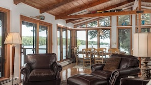 Un amplio salón con sofás de cuero, una mesa de comedor y grandes ventanales con vistas a un lago.