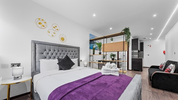 Et moderne hotelværelse med en stor seng, et natbord, en lænestol, en sofa og et skrivebord med stol.
