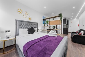 A modern hotel room with a large bed, a bedside table, a chair, a sofa, and a desk with a chair. - Bright Studio Retreat in Golders Green (London)