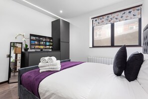 A modern bedroom with a bed, a television, and a window with blinds. - Bright Studio Retreat in Golders Green (London)