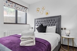 A hotel room with a large bed, a window with blinds, a bedside table with a lamp, and decorative wall art. - Bright Studio Retreat in Golders Green (London)