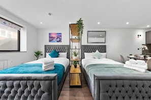 A modern hotel room with two beds, a small table, and a mirror.