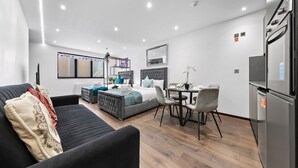 A modern hotel room with a bed, a sofa, a dining table with chairs, and a kitchen area with a refrigerator. - Cosy Golders Green Studio With Modern Amenities (London)