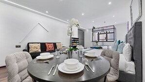 A modern dining area with a round table set for four, surrounded by upholstered chairs. - Cosy Golders Green Studio With Modern Amenities (London)