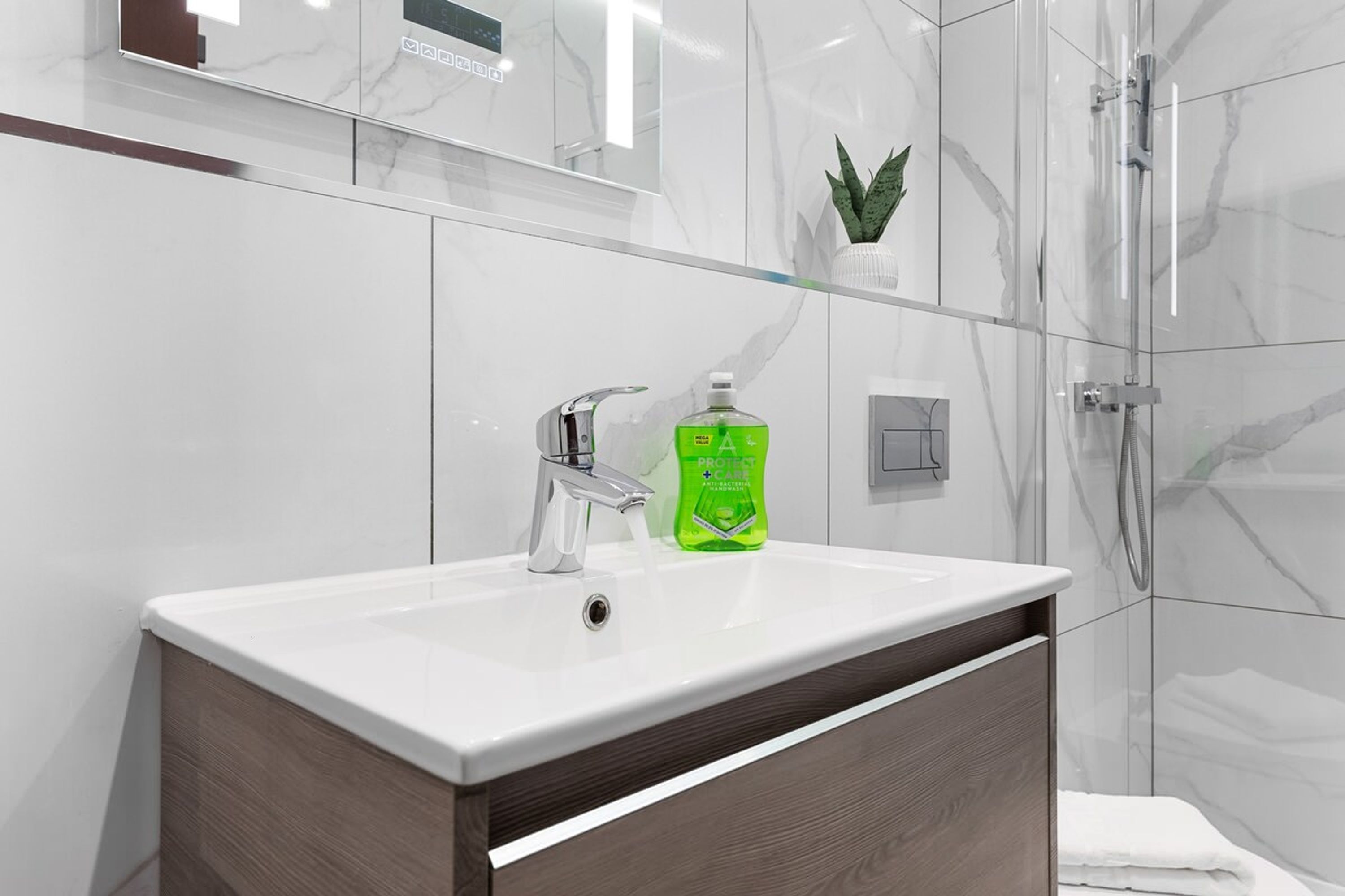 A modern bathroom with a white sink, chrome faucet, and a green bottle of liquid soap.