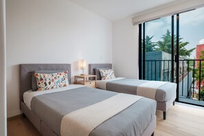 A hotel room with two beds, a nightstand, a lamp, and a large window with a view of buildings and trees. - Chilpancingo 57 Unit 606 (Mexico City)