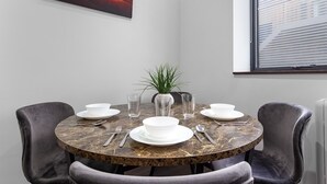 A round dining table with a marble top, surrounded by four grey upholstered chairs. A white vase with green plants is placed in the center. - Stylish Studio in Golders Green Central Location (London)