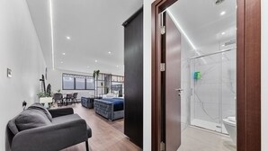 A modern hotel room with a sofa, a dining area, and a shower. - Stylish Studio in Golders Green Central Location (London)