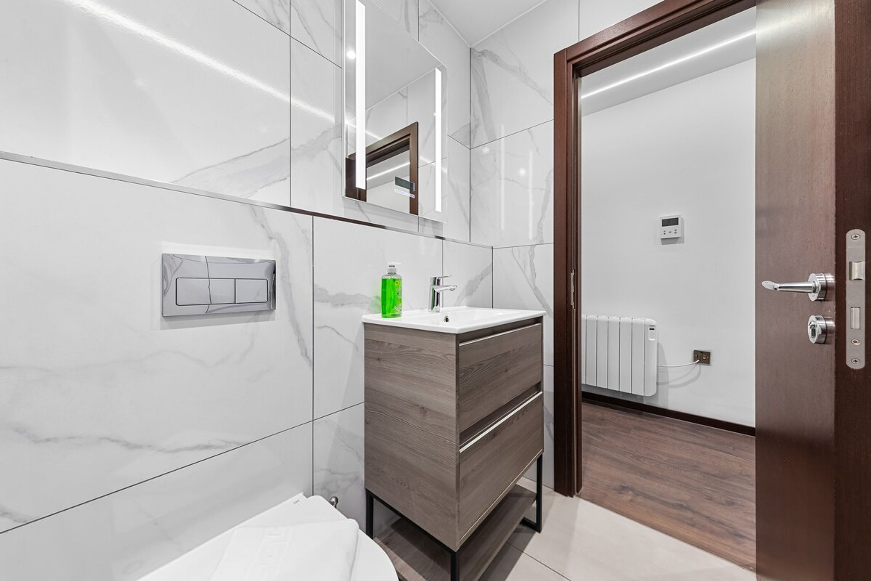 Un baño moderno con pared de mármol, tocador de madera, un espejo y una puerta que da a la zona de la ducha.