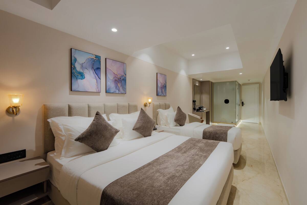 Une chambre d’hôtel avec deux lits, une grande fenêtre et une salle de bain visible à travers une porte ouverte.