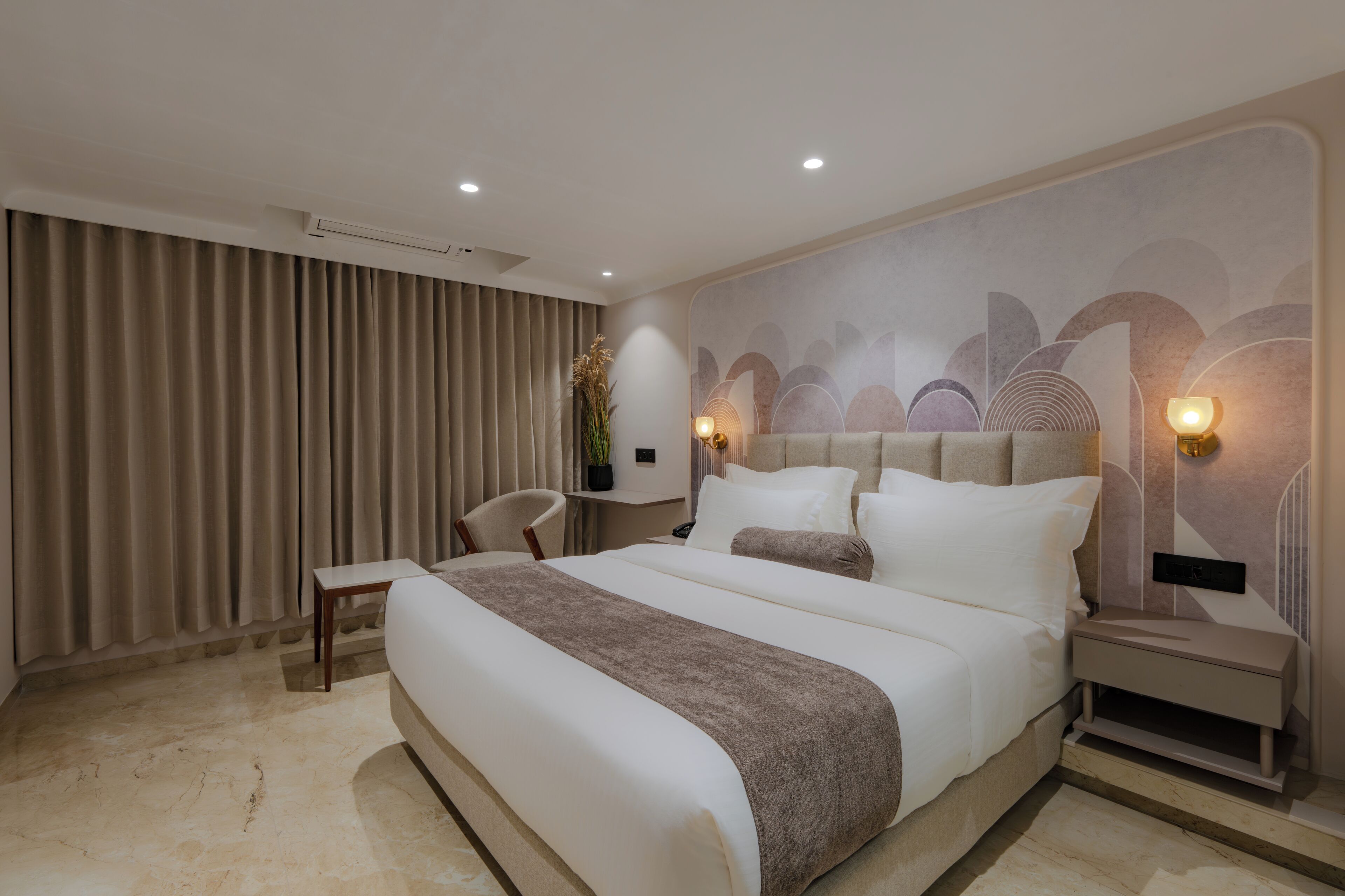 Habitación de hotel moderna con una cama grande, una mesita de noche, una silla y un detalle decorativo en la pared.
