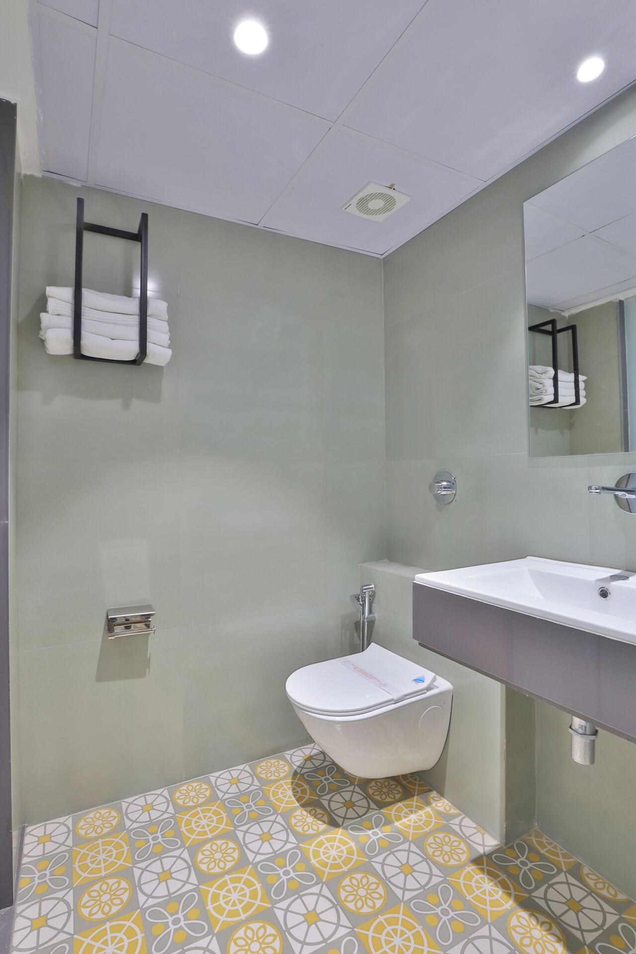 Un bany modern amb un vàter blanc, un lavabo amb mirall i un suport per tovalloles.