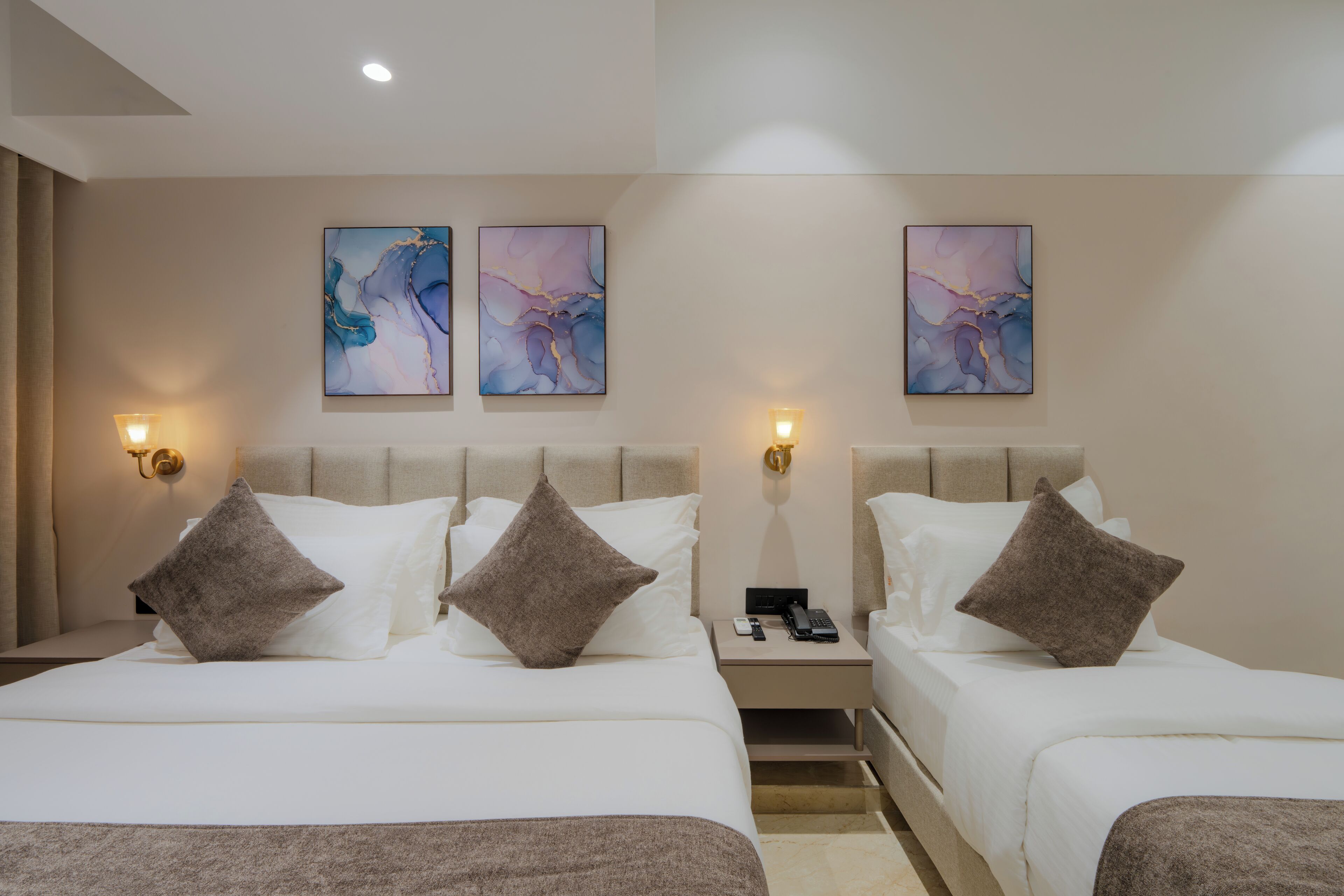 Habitación de hotel con dos camas, cada una con ropa de cama blanca y almohadas marrones. Hay tres apliques de pared a cada lado de las camas.