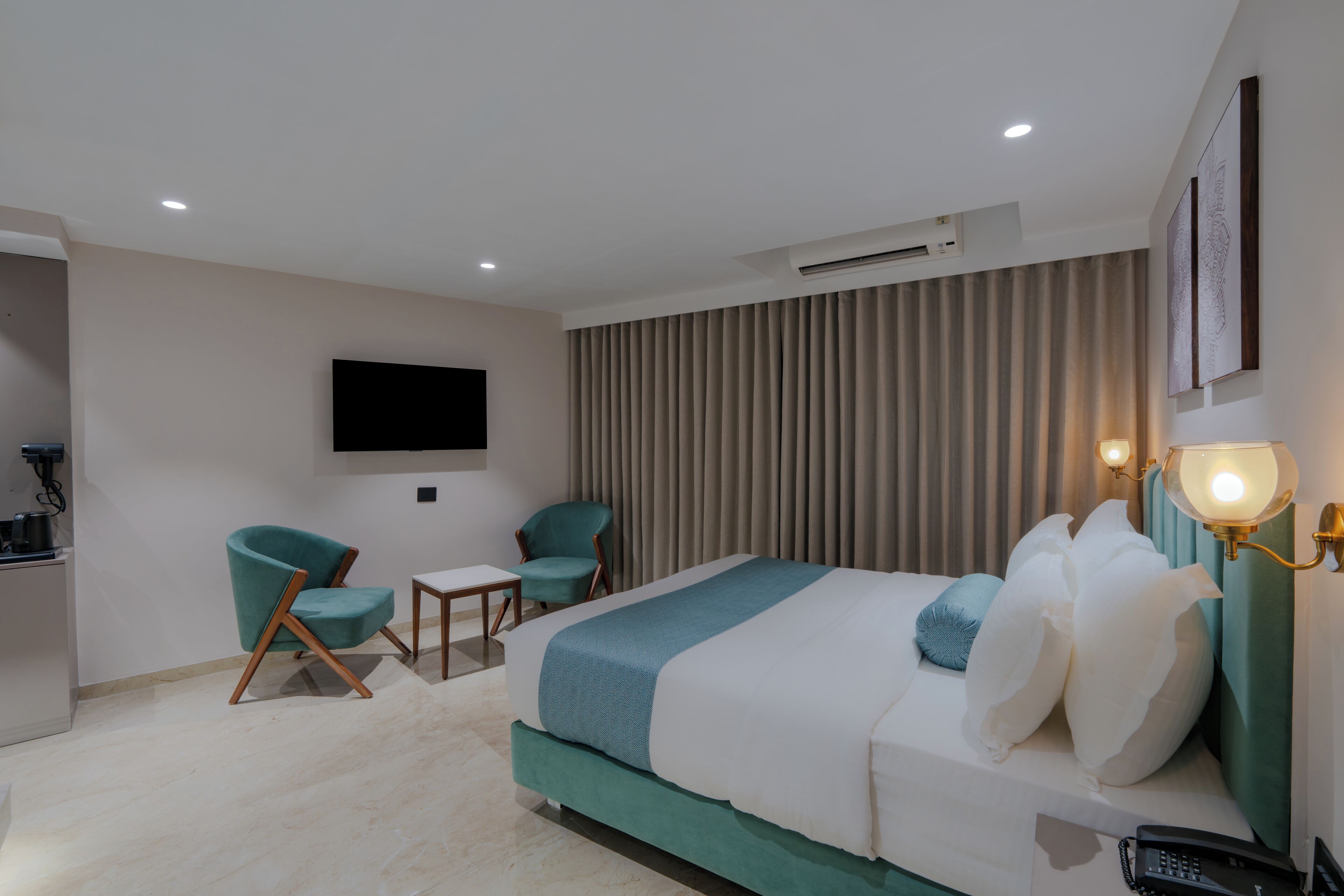 Een hotelkamer met een bed, twee stoelen, een klein tafeltje, een televisie en een wandlamp.