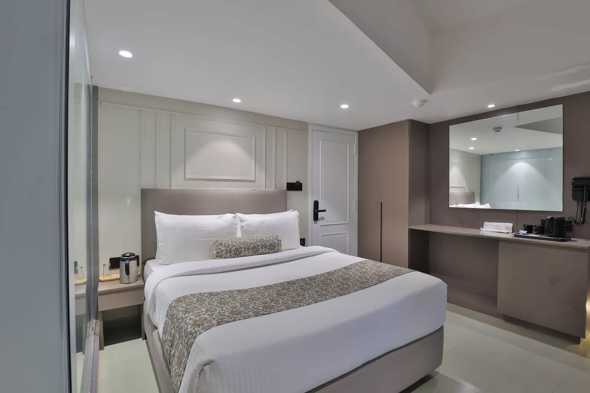 Une chambre d’hôtel moderne dotée d’un grand lit, de tables de chevet, d’un bureau intégré, d’un miroir et d’une machine à café.