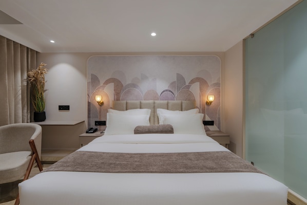 A modern hotel room with a large bed, bedside tables, a chair, and a decorative wall. - Hotel The Grand Suites (Ahmedabad)