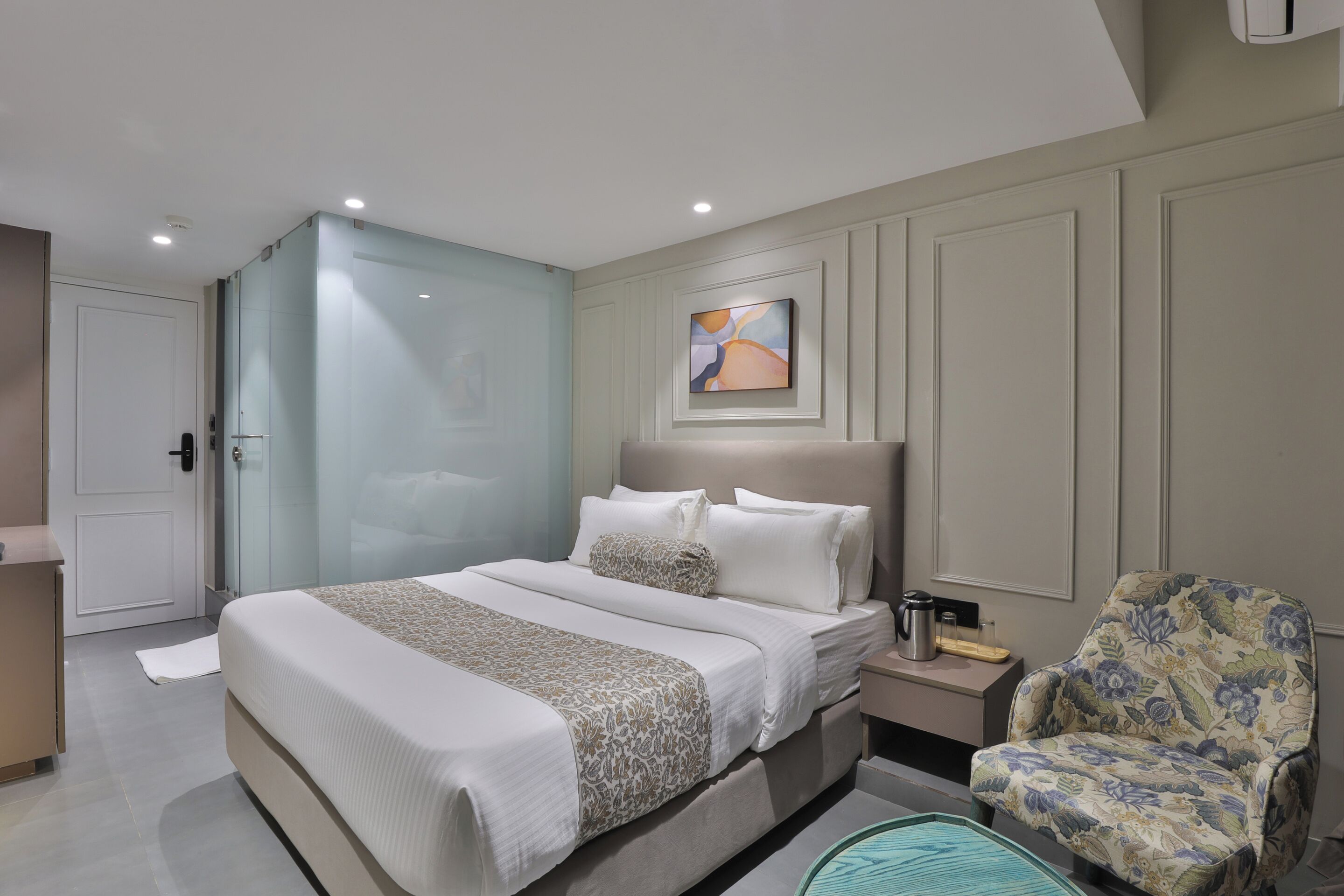 Habitación de hotel moderna con una cama grande, una mesita de noche, una silla y un cuadro en la pared.
