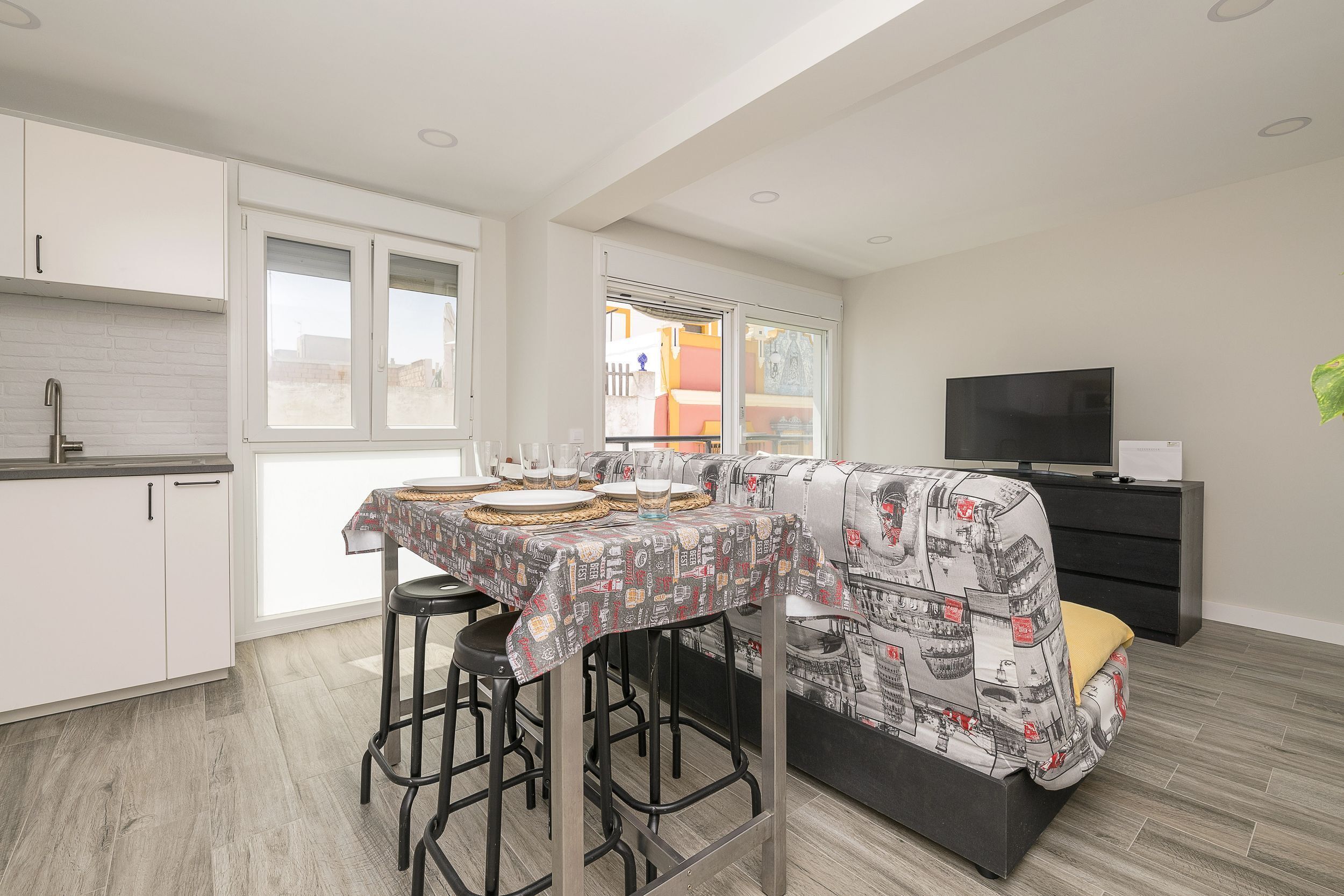 Een moderne keuken met witte kasten, een eettafel gedekt met borden en glazen, een barkruk en een bank met een gestreept hoesje.
