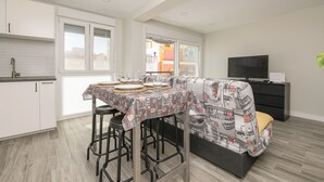 Una cocina moderna con armarios blancos, una mesa de comedor con platos y vasos, un taburete de bar y un sofá con un estampado.