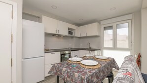Una cocina compacta con armarios blancos, un microondas y un comedor con mantel estampado.