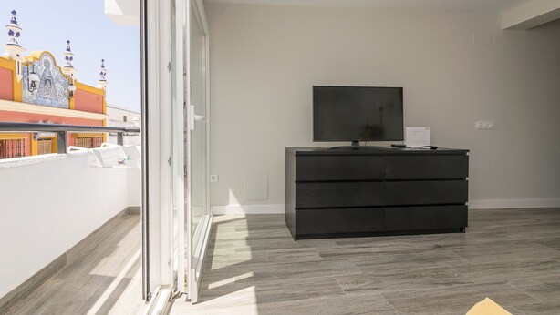 Una habitación moderna con puerta de vidrio corredera que da a un balcón, un mueble de televisión negro y suelo de baldosas.