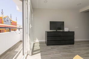 Une chambre moderne dotée d’une porte-fenêtre coulissante donnant sur un balcon, d’un meuble TV noir et d’un sol carrelé.
