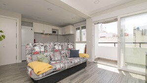 Una sala moderna con sofá, cocina y una amplia puerta corrediza de vidrio a un balcón.