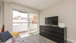 Un dormitorio con cama, televisor, cómoda y puerta corrediza de vidrio que da a un balcón.