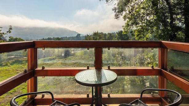 A balcony with a glass table and two chairs, overlooking a lush landscape with trees and a distant mountain range. - RentPlanet - Holiday Mountain Residence (Swieradow-Zdroj)