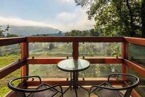 A balcony with a glass table and two chairs, overlooking a lush landscape with trees and a distant mountain range. - RentPlanet - Holiday Mountain Residence (Swieradow-Zdroj)