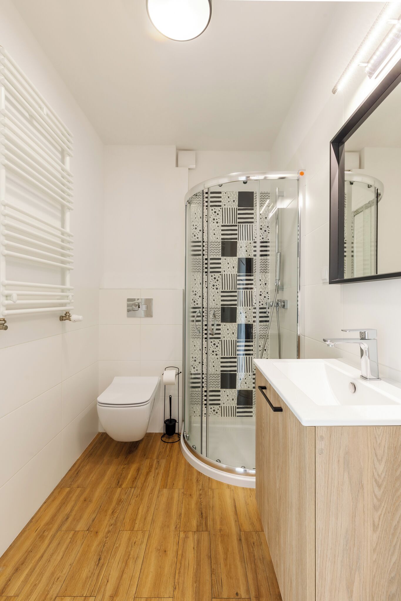 Une salle de bain moderne avec une douche à parois de verre, des toilettes blanches, un meuble-lavabo en bois et un miroir.