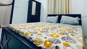 A bedroom with a bed, a wardrobe, a mirror, a window with curtains, and an air conditioning unit. - Explore Private Pool Villa Varkala (Varkala)