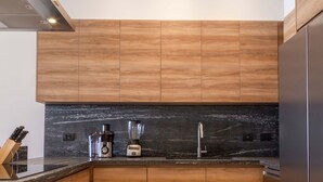 Eine moderne Küche mit Holzausstattung, einer schwarzen Arbeitsplatte, einem Edelstahlkühlschrank und einem eingebauten Herd.