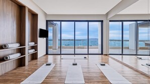 Ein modernes Yogastudio mit Holzboden, großen Fenstern mit Meerblick und einem an der Wand montierten Flachbildfernseher.