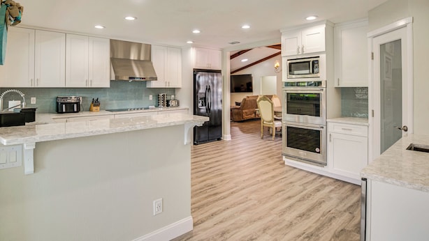 Ett modernt kök med vita skåp, en rostfri köksfläkt, en inbyggd mikrovågsugn och en varmluftsugn med två ugnar.