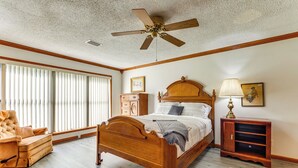 A bedroom with a wooden bed, a ceiling fan, a nightstand, a lamp, and a window with blinds. - Pensacola Home ~ 13 Mi to Perdido Bay! (Pensacola)