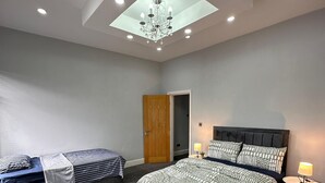 Une chambre avec un puits de lumière, un lit avec une literie à motifs, un banc recouvert d’un tissu à rayures et une table de chevet avec une lampe.