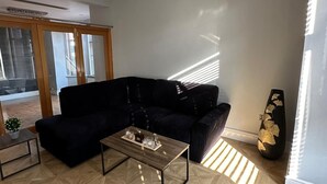 Un salon moderne avec un canapé noir, une table basse en bois et un pouf noir.