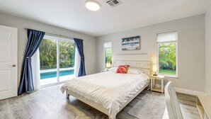 A bedroom with a large bed, a nightstand, a lamp, a window with a view of greenery, and a door leading to a balcony. - 2 Mi to Deerfield Beach: Home w/ Outdoor Oasis! (Deerfield Beach)