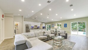 A spacious living room with a large sectional sofa, a glass coffee table, and a view of the backyard through large sliding glass doors. - 2 Mi to Deerfield Beach: Home w/ Outdoor Oasis! (Deerfield Beach)