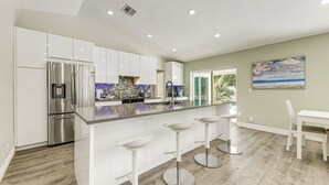 A modern kitchen with white cabinetry, a stainless steel refrigerator, and a large island with bar stools. - 2 Mi to Deerfield Beach: Home w/ Outdoor Oasis! (Deerfield Beach)