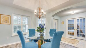 A dining area with a glass table, four blue chairs, a chandelier, and a vase with flowers. - 4 Mi to Beach: Family-friendly Home in Navarre (Navarre)
