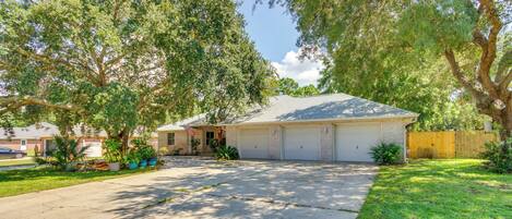 A residential house with a garage, driveway, and surrounding trees.