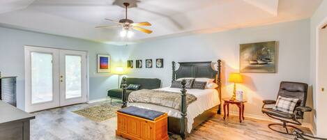 A bedroom with a bed, a chair, a nightstand, a ceiling fan, and a door.