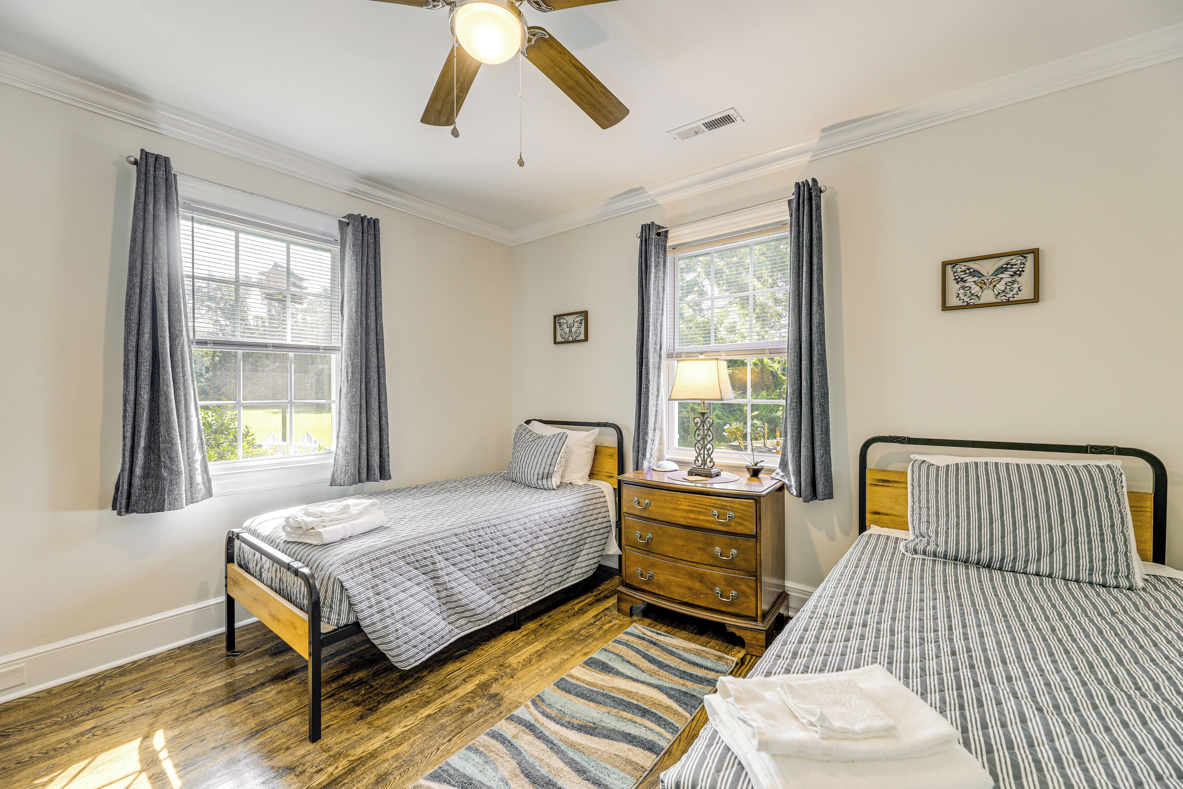 A bedroom with two beds, a wooden dresser, a ceiling fan, and a window with curtains.