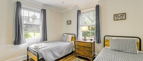 A bedroom with two beds, a wooden dresser, a ceiling fan, and a window with curtains.